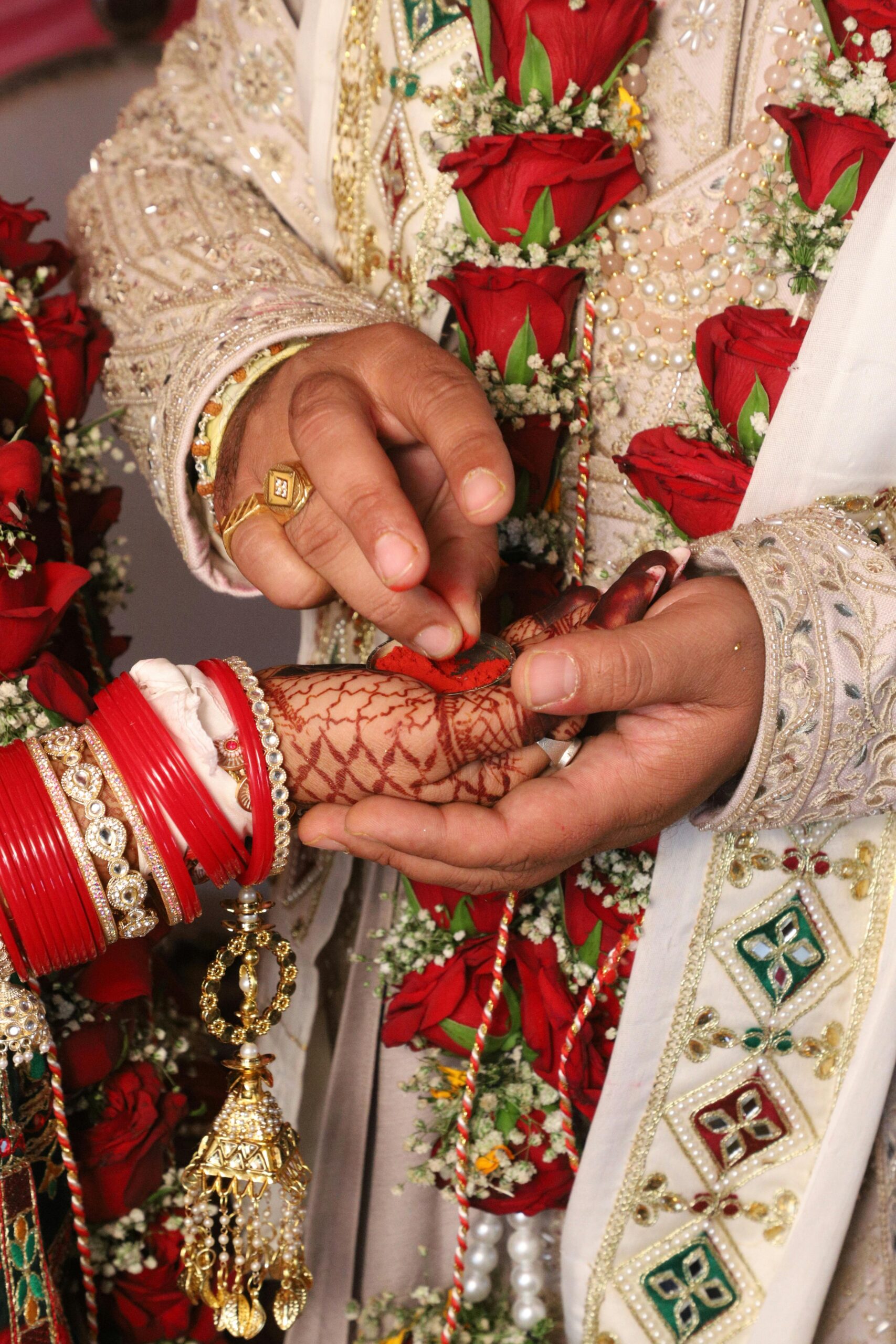 Close-up of an Indian wedding ceremony with bride and groom's hands adorned with jewelry and henna.